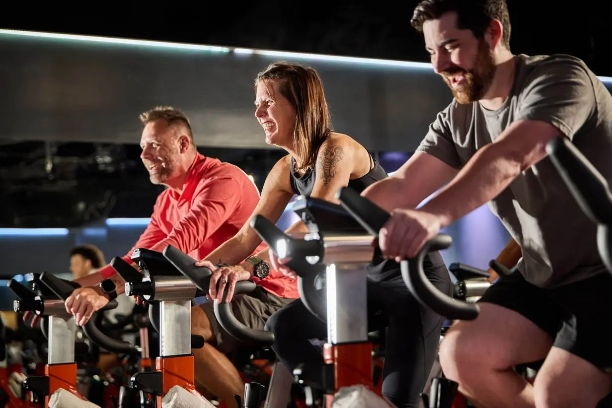 Members enjoying an energetic group cycling class at Village Clubs Camelback, in a bright, modern indoor studio.