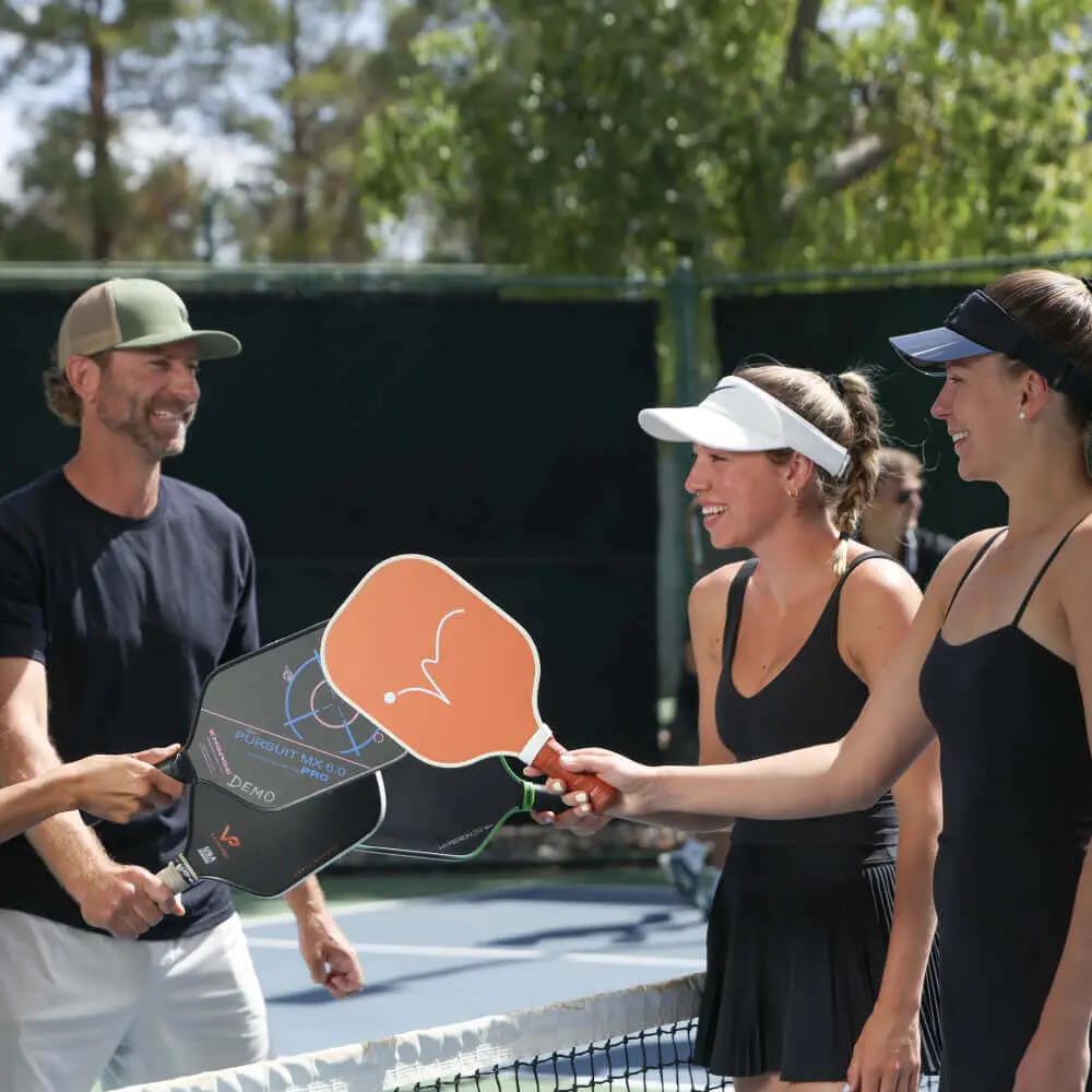 Players at Village Clubs Camelback enjoy a pickleball match, smiling and tapping paddles in sportsmanship on the court.