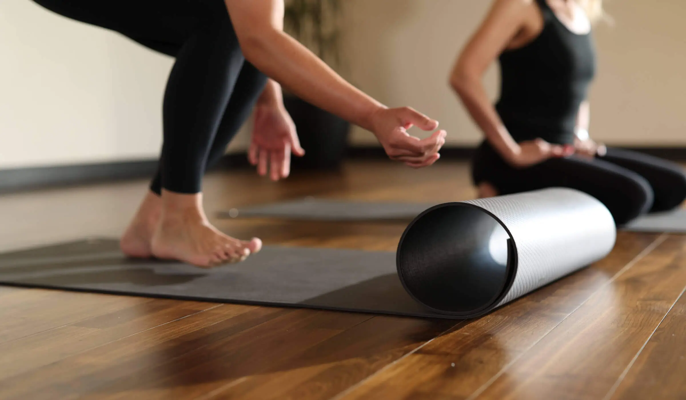 Two people prepare for yoga at Village Clubs Camelback, stretching on mats in a bright studio with wood floors.