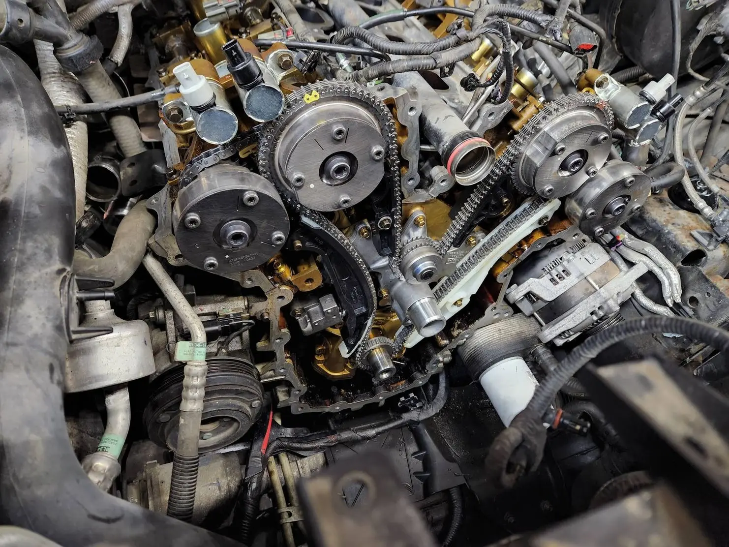 Disassembled engine bay showing timing chains, cam phasers, and accessory components