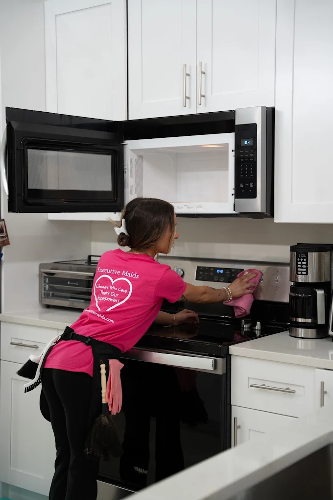 Young house cleaner performing detailed cleaning on kitchen stove in Delray Beach, FL house
