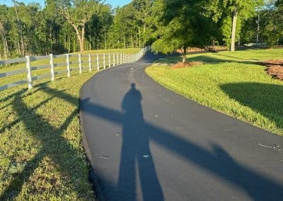 Curved asphalt park path along a white fence line