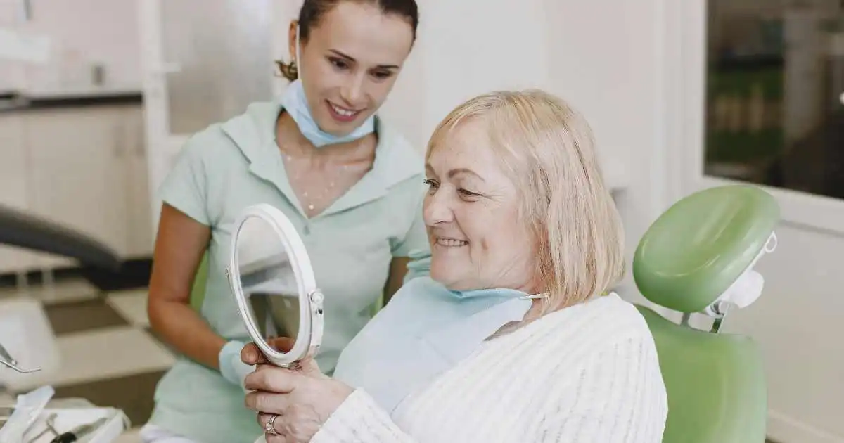 dentures-bone-loss-senior-care senior woman with dentist holding a mirror while she checks the fit of her dentures
