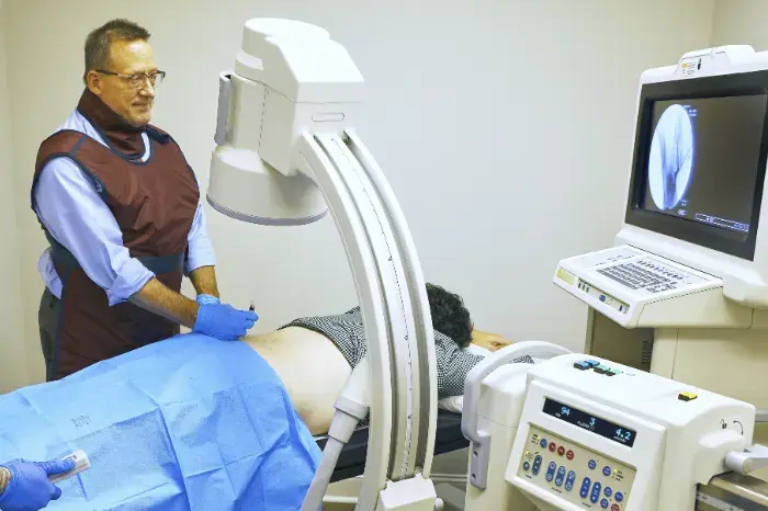 Medical professional in a lead apron positions a patient for a C-arm X-ray scan.