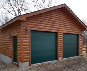 Custom two-car garage with log siding, green garage doors, and carriage-style wall lanterns built by Quality Log Home Builders in North Carolina