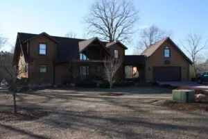Large custom log home with attached garage, covered porch, and multiple gabled dormers on a wooded lot in North Carolina