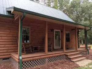 Close-up of a log cabin front porch with rocking chairs, green metal roof, and wood deck surrounded by pine trees in North Carolina