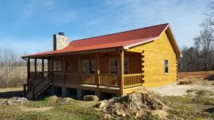 Newly built log cabin with red metal roof, stone chimney, and wrap-around covered porch on a rural North Carolina property