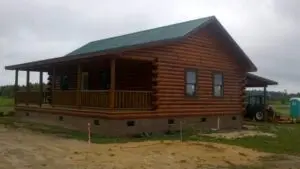 Newly constructed log cabin with green metal roof and covered front porch on a rural property in North Carolina.