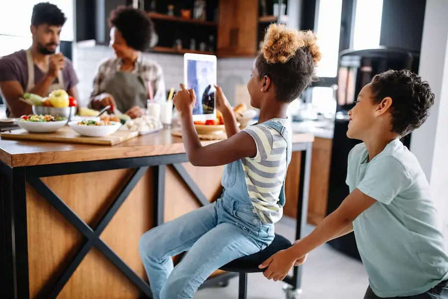 happy family in kitchen, children taking photo of parents who are cooking