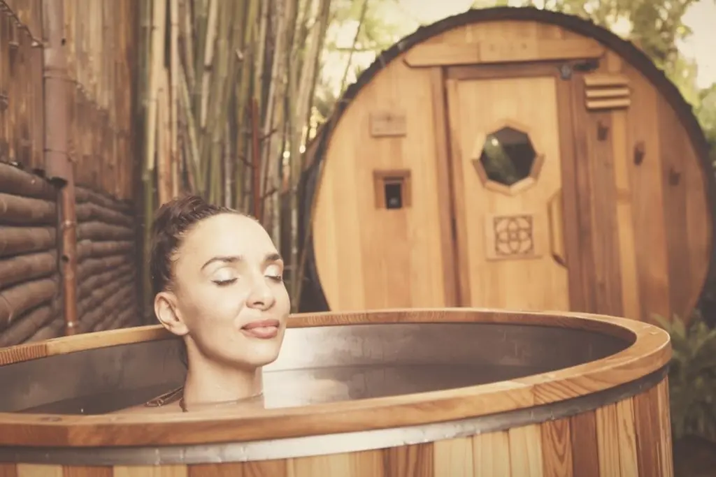 Woman in an outdoor cedar cold plunge with a barrel sauna behind her, for contrast therapy at SILA Miami