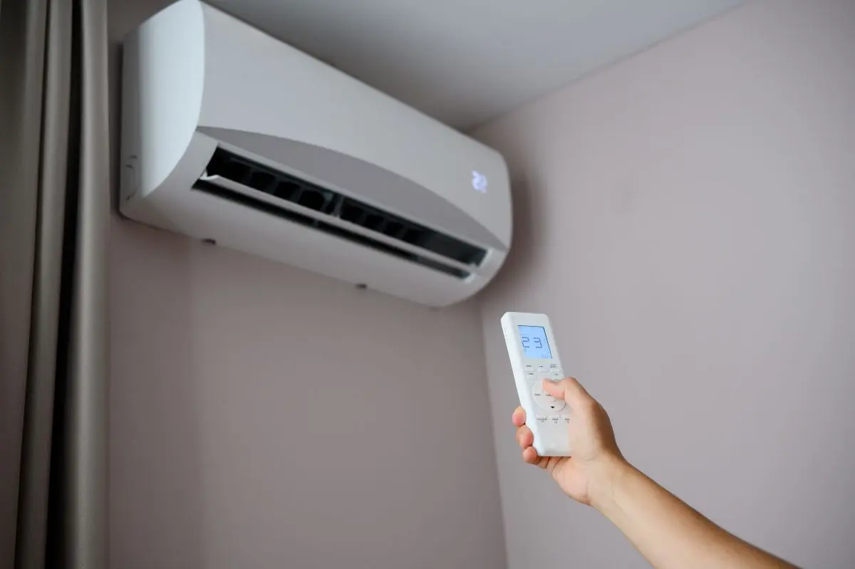Man holds remote control in front of an air conditioner, adjusting its temperature