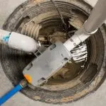 Sump pump installation in a basin with pipes and water, showcasing B&L Plumbing’s flood management solutions.