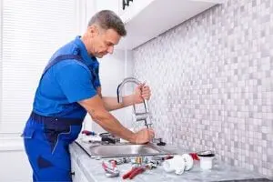 Professional plumber repairing a kitchen sink with tools, emphasizing emergency plumbing services and expertise in resolving urgent plumbing issues.