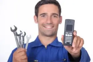 Smiling plumber in blue uniform holding wrenches and a phone, representing emergency plumbing services and quick response for plumbing issues.