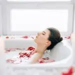 Woman in a bathtub with rose petals, bright natural light, perfect for bathroom upgrades by B&L Plumbing.