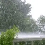 Heavy rain blurs greenery and a deck, depicting plumbing risks during spring rains for B&L Plumbing’s services.