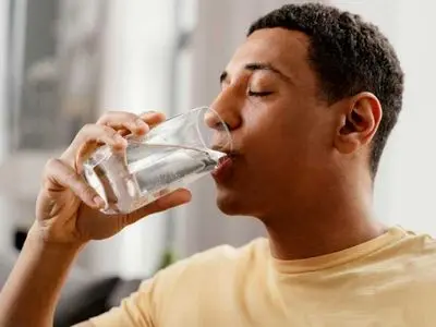 Person drinking a glass of clear water, emphasizing the benefits of safe and better-tasting drinking water from a filtration system.