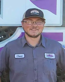Chase Schexnayder, B&L Plumbing technician, smiling in work uniform with name tag, against a colorful background, showcasing his plumbing expertise and friendly demeanor.