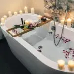 Luxurious bathtub with rose petals, candles, and wooden bath tray for bathroom upgrades by B&L Plumbing.