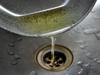 Pouring cooking oil into a kitchen sink drain, highlighting improper disposal practices that can lead to plumbing clogs.