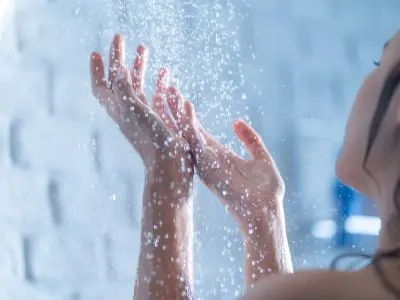 Woman enjoying a warm shower with water droplets falling on her hands, illustrating the importance of consistent hot water supply from a functioning water heater.