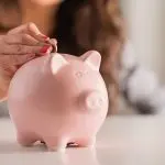 Female hand inserting a coin into a pink piggy bank, symbolizing saving money for improved home water filtration systems.