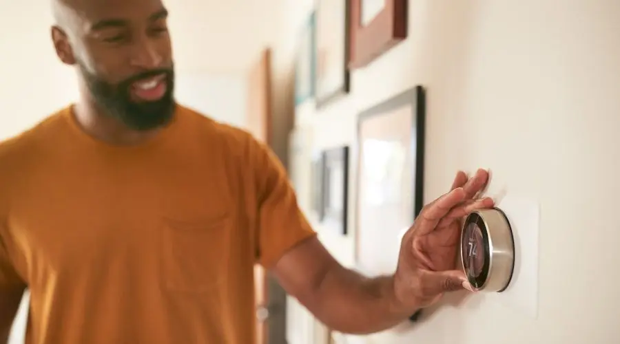 Man adjusting a smart thermostat on a wall, showcasing modern climate control technology for energy efficiency and comfort.