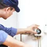 Male technician in work uniform adjusting a thermostat in a Colorado Springs home for efficient water heater operation.