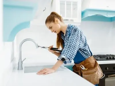 Woman plumber repairing kitchen faucet, showcasing female representation in the plumbing industry during Women's History Month.