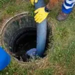 Two plumbers using a hose near a well for sewer maintenance, wearing bright yellow gloves in Colorado Springs.