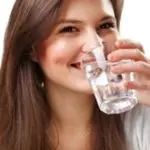 Young woman smiling while drinking water, promoting hydration, wellness, and water filtration solutions by B&L Plumbing.
