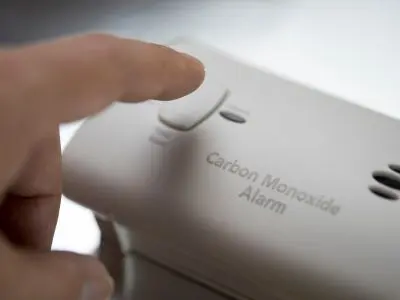 Hand pressing the test button on a carbon monoxide alarm, highlighting the importance of safety measures against carbon monoxide leaks in homes.