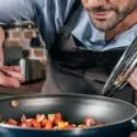 Man cooking in a kitchen, focusing on saut&eacute;ing vegetables in a pan, emphasizing kitchen plumbing safety and cooking practices during holiday meal preparations.