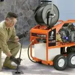 A man with gloves operates a mobile cleaning machine for outdoor plumbing maintenance at B&L Plumbing services.