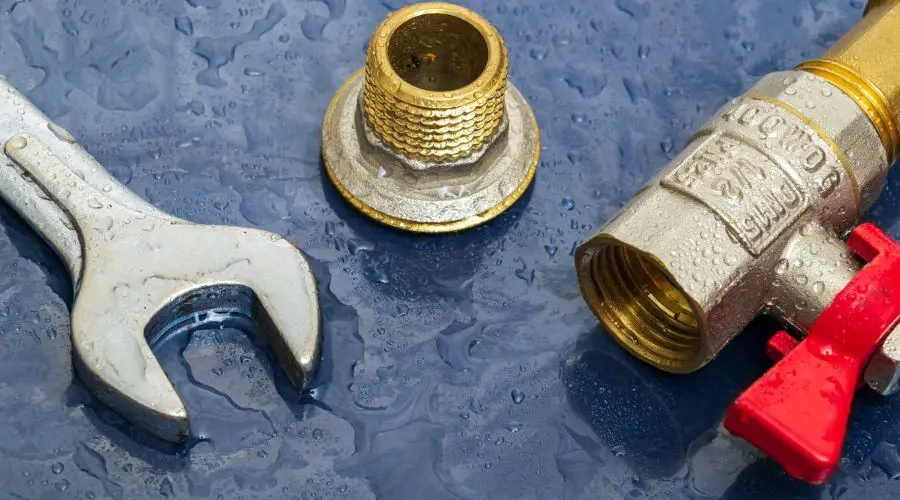 Wrench, brass fitting, and valve on wet surface, representing plumbing tools and components relevant to plumbing services and repairs.