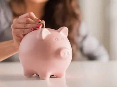 Person placing a coin into a pink piggy bank, symbolizing savings and financial benefits of installing a water filtration system.