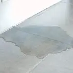 Water puddle on light-colored tiled floor indicating potential plumbing issues related to slab leaks by B&L Plumbing.
