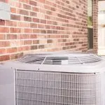 Air conditioning unit installed outside a brick wall, emphasizing the importance of regular maintenance and air filter changes for efficient cooling and indoor air quality.