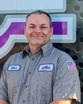 Michael Woods, certified plumber at B&L Plumbing and Heating, wearing a work uniform with name tag and American flag, smiling in front of a branded backdrop.
