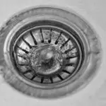 Circular metal sink drain cover with textured design and knob, showcasing essential plumbing infrastructure by B&L Plumbing.