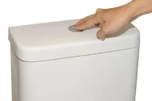 Hand pressing flush button on low-flushing toilet, emphasizing water conservation and efficient bathroom plumbing solutions.