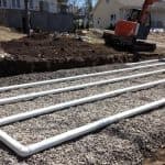 Excavator on gravel surface with PVC pipes, highlighting plumbing installation for septic systems by B&L Plumbing.
