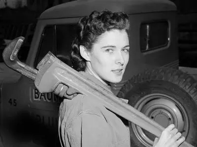 Lillian Ann Baumbach, first female master plumber, holding a large pipe wrench, showcasing her role in the plumbing industry against a vintage truck backdrop.