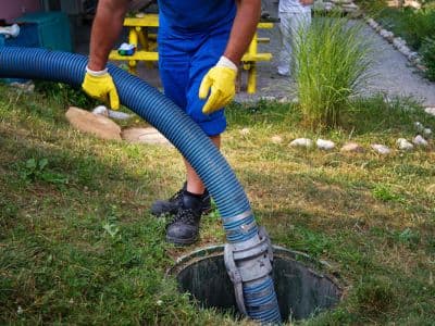 Septic system maintenance with technician using vacuum hose to pump septic tank in residential yard.