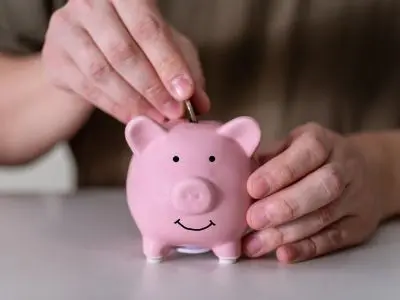 Person inserting a coin into a pink piggy bank, symbolizing savings and financial management related to smart thermostat installation benefits.
