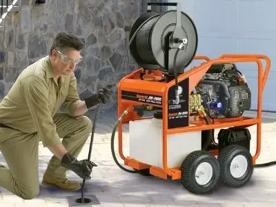 Plumber using hydro-jetting equipment to clear outdoor clogged pipes, emphasizing professional plumbing services and maintenance.