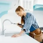 Female plumber with tools in modern kitchen, showcasing B&L Plumbing's commitment to women's contributions in plumbing.