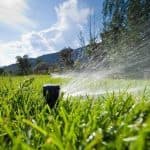 Lawn sprinkler watering grass under a clear sky, showcasing outdoor plumbing solutions by B&L Plumbing.