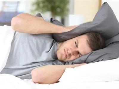 Man covering his ears with a pillow, showing frustration from loud noises, symbolizing issues related to noisy water heaters.